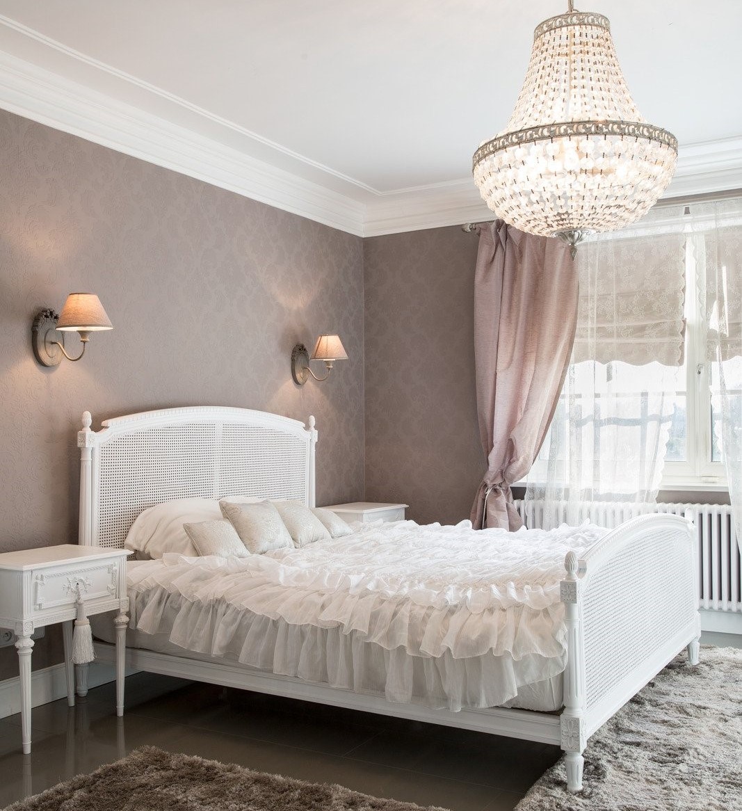 kryształowy żyrandol w sypialni, białe ażurowe łóżko, pudrowo różowe ściany